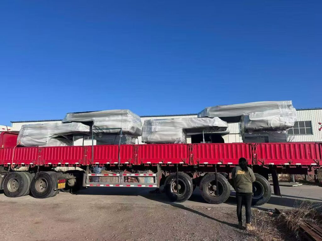 Side view of a long flatbed semi-trailer loaded with multiple white slide-in truck campers ready for wholesale delivery.