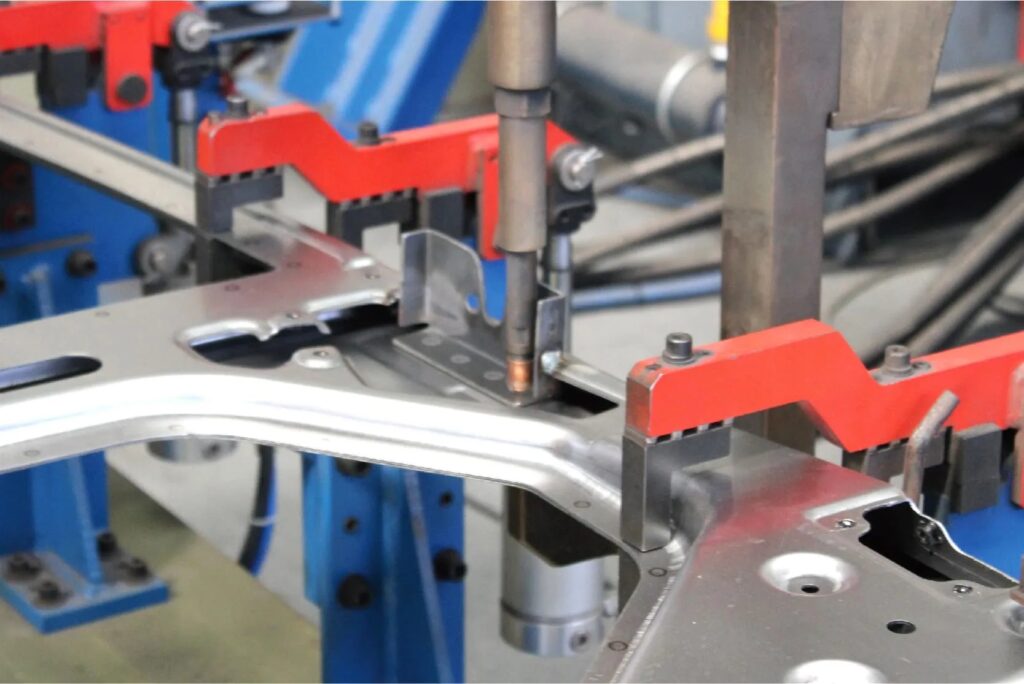 Close-up view of a robotic spot welding tool joining metal sections of a slide-in camper chassis with high pressure and precision.