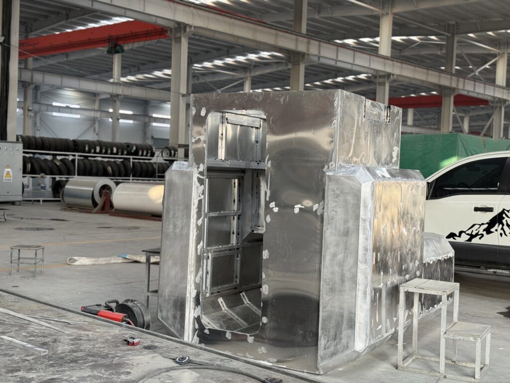 Welding workshop showing the raw metal body shell of a slide-in camper before insulation and painting.
